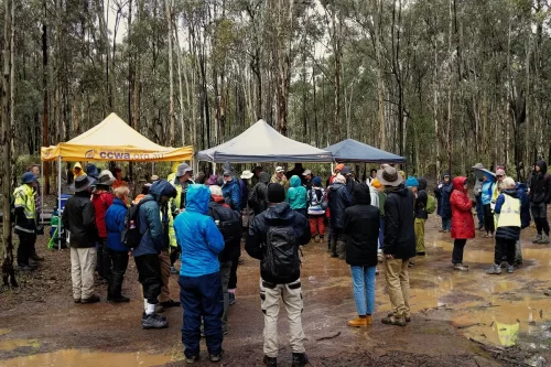 multiple people gathered in a very muddy, wet area, ready for instruction. Tents in the background. Photo by Amber Bateup